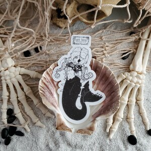 Gothic pirate mermaid sticker by artist White stag for Paper Haunt Stationery & Co in a sea shell on sand with a skull and skeleton hands reaching through a fish net.