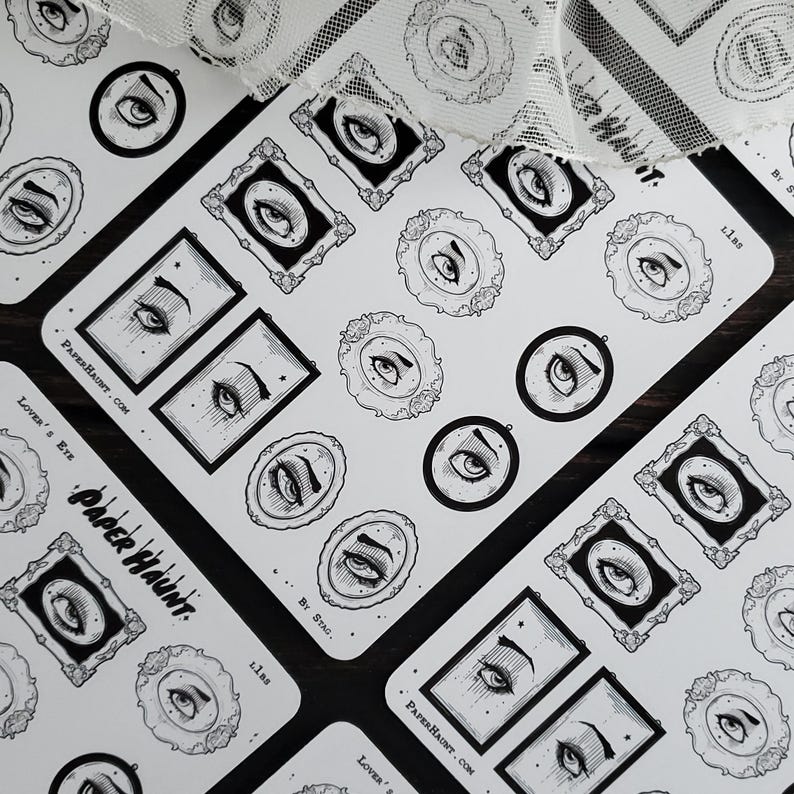 May include: A sheet of stickers featuring black and white illustrations of eyes in ornate frames. The stickers are on a white background and have the text "Paper Haunt" and "Lover's Eye" printed on them.