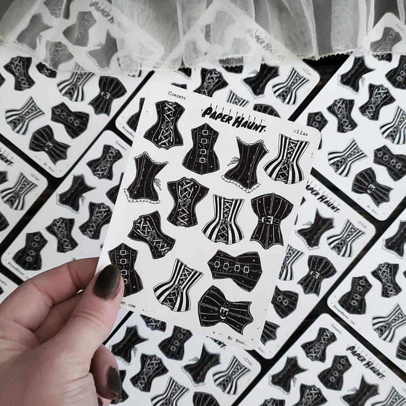 May include: A sheet of black and white stickers featuring various corset designs. The stickers are on a white background and have the text "Paper Haunt" and "By Sting" printed on them.