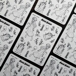 May include: A sheet of black and white stickers featuring a spooky haunted garden theme. The stickers include a ghost, a tombstone, flowers, and a girl in a white dress. The sheet is labeled "Paper Haunt" and "Haunted Garden".