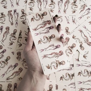 a hand holding creepy cute goth mermaid skeleton stickers