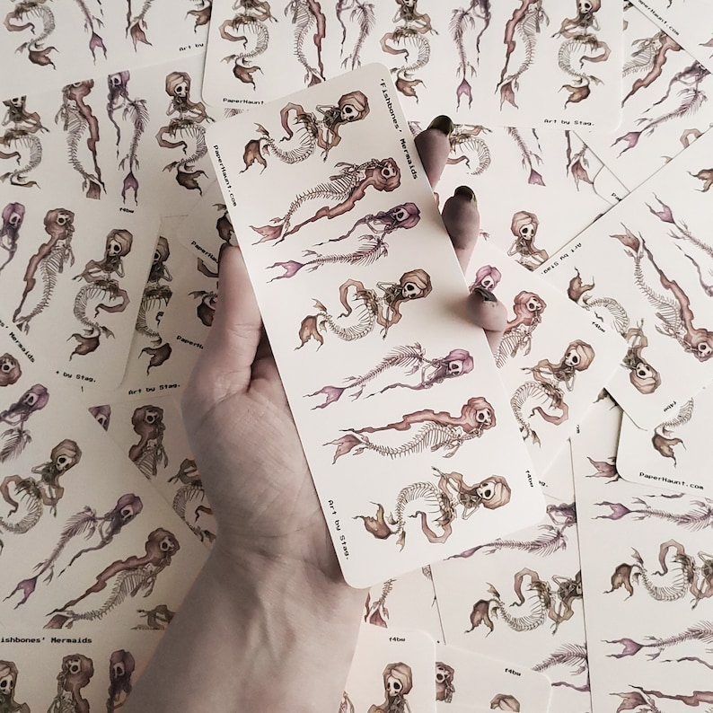 a hand holding creepy cute goth mermaid skeleton stickers