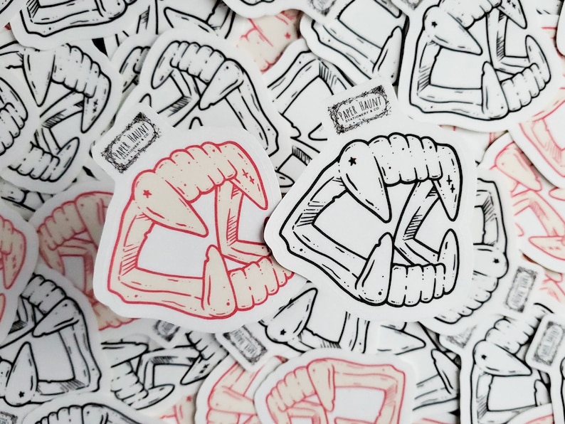 May include: A set of black and white stickers featuring a pair of fangs. The stickers are printed with the text "Paper Haunt".