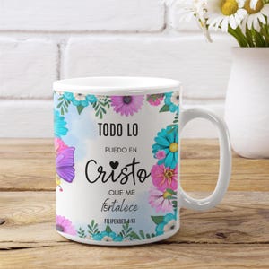 Op de afbeelding: Witte keramische mok met een bloemenontwerp in blauw, roze en paars. De mok toont de Spaanse tekst "TODO LO PUEDO EN CRISTO QUE ME fortalece FILIPENSES 4:13" in zwart schrift.