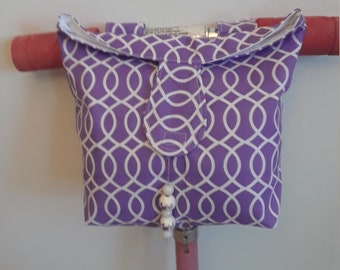 May include: A purple scooter bag with a white oval pattern, attached to the handlebars. The bag has a flap closure and a beaded charm. The bag's design features a white interlocking oval pattern on a purple background.