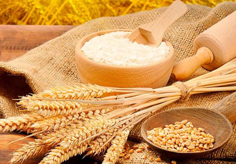 May include: A wooden bowl filled with white flour, a wooden spoon, a rolling pin, and wheat stalks on a burlap background.