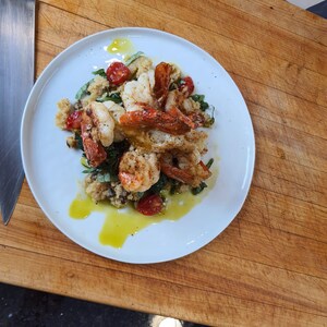 May include: A white plate with a serving of shrimp, couscous, and cherry tomatoes. The shrimp are cooked and have a light brown color. The couscous is white and fluffy. The cherry tomatoes are red and juicy.
