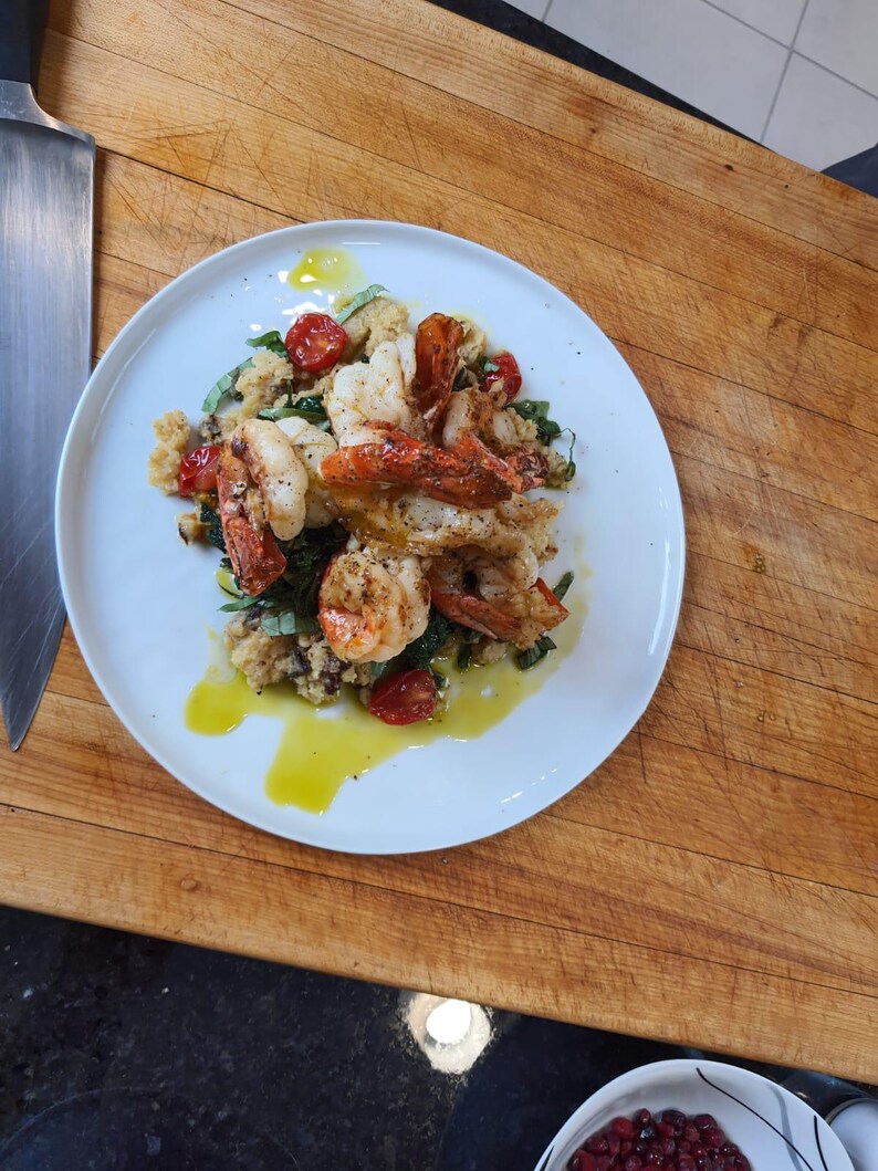May include: A white plate with a serving of shrimp, couscous, and cherry tomatoes. The shrimp are cooked and have a light brown color. The couscous is white and fluffy. The cherry tomatoes are red and juicy.