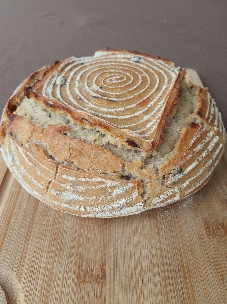 May include: A round loaf of sourdough bread with a spiral pattern on top. The bread is on a wooden chopping board.