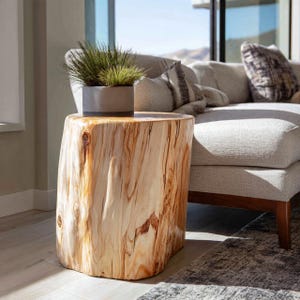May include: A natural wood side table with a cylindrical shape and a light brown finish. The table has a rough, textured surface and a live edge. A potted plant with green grass sits on top of the table.