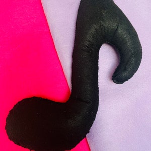 May include: A black felt musical note shaped like a treble clef, lying on a pink and purple surface.