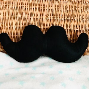 Pu&ograve; includere: Un cuscino di peluche nero a forma di baffi. Il cuscino ha la forma di un baffo ed &egrave; fatto di tessuto morbido e soffice.