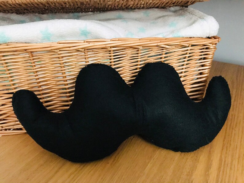 Pu&ograve; includere: Un cuscino a forma di baffi in feltro nero. Il cuscino ha due estremit&agrave; arrotondate grandi e un centro curvo pi&ugrave; piccolo.