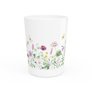May include: White tumbler with a watercolour design of wildflowers and butterflies in shades of pink, purple, yellow, and green. The floral border wraps around the base of the tumbler.