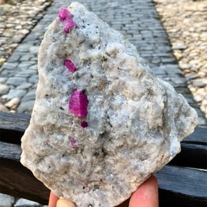 May include: A rough, white rock with several small, bright pink ruby crystals embedded in it.