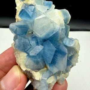 May include: A cluster of translucent blue fluorite crystals with sharp geometric facets and pale yellow mineral inclusions. The mineral specimen features a jagged, crystalline structure with varying shades of deep and light blue throughout the formation.
