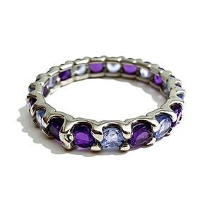 May include: A silver ring set with alternating purple and light blue gemstones. The ring has a continuous band of oval-cut stones, creating a full eternity design. The gemstones are set in a silver band.