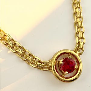 以下が含まれることがあります： 赤い宝石のペンダントが付いたゴールドのネックレス。ペンダントは金のフレームで囲まれています。チェーンは二重のゴールドリンクです。