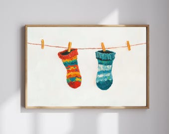 May include: A framed painting depicts two colorful socks hanging on a clothesline. One sock is red, orange, yellow, and blue. The other is blue and white. The background is white.