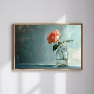 May include: A framed art print featuring a peach-colored rose in a clear glass jar. The rose has green leaves and is set against a teal and blue background. The artwork is displayed in a light brown wooden frame.