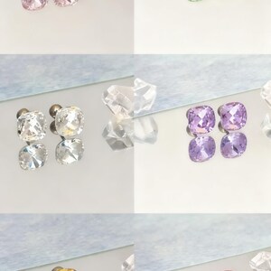 May include: A collection of square-cut stud earrings in various colors, including pink, green, clear, purple, gold, and red. The earrings are displayed on a reflective surface, showcasing their facets and sparkle. The image highlights the different color options available.