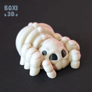 Puede incluir: Una figurita de araña blanca impresa en 3D con ojos negros. La araña tiene un cuerpo redondeado y bulboso y ocho patas.