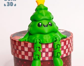 Puede incluir: Una figurita de árbol de Navidad verde con una estrella amarilla en la parte superior, sentada en una caja de regalo a cuadros rojos y blancos. El árbol tiene una cara sonriente y piernas articuladas.