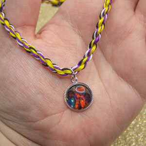 May include: A necklace with a purple, yellow, and black braided cord and a round pendant with a colorful galaxy image.