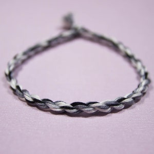 May include: A braided bracelet with black, white, and gray threads.