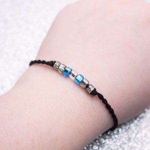 May include: A black string bracelet with blue and silver beads.
