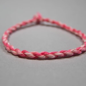 Puede incluir: Un brazalete trenzado de color rosa y blanco hecho de hilo.