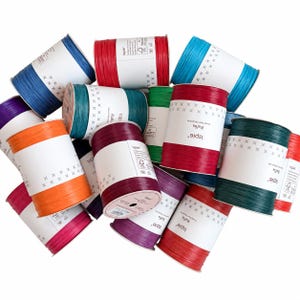 May include: A collection of Ispie brand raffia yarn spools in various colors including red, blue, orange, purple, green, and teal. Each spool features a white paper label with the text Ispie, Raffia, and a pattern of small black crosses.