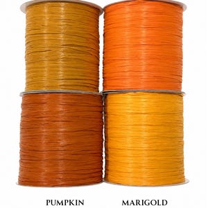 May include: Four spools of raffia ribbon arranged in a square grid. The top left spool is labeled GINGER COLOR 76, the top right is BRIGHT ORANGE COLOR 21, the bottom left is PUMPKIN COLOR 69, and the bottom right is MARIGOLD COLOR 60.