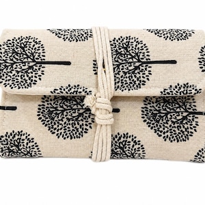 May include: A rectangular fabric roll-up case featuring a repeating black tree pattern on a beige background. The case is secured with a thick, off-white cord that wraps around the center and ties in a knot, keeping the folded flap closed.