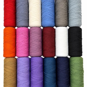 May include: Eighteen cylindrical spools of cord arranged in a grid of three rows and six columns. The spools feature a variety of solid colors including red, gray, cream, blue, orange, pink, purple, burgundy, white, black, tan, and olive green.
