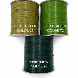 May include: Three spools of raffia ribbon in shades of green. The top left spool is labeled OLIVE GREEN COLOR 25, the top right is LEAF GREEN COLOR 72, and the bottom center spool is labeled SPIRULINA COLOR 26. Each spool features a textured surface.