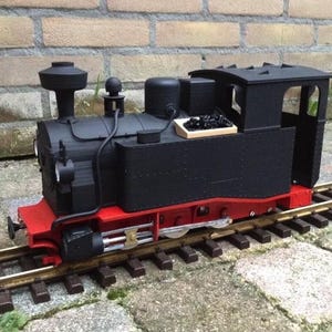 May include: A black model train engine with red wheels and a small wooden box filled with black coal. The engine is on a set of train tracks.