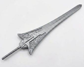 May include: A silver-colored sword featuring a wide, pointed blade with intricate embossed scrollwork patterns near the hilt. The sword has a long, slender, ribbed handle and a flared guard section that transitions into a tapered, sharp-edged blade.