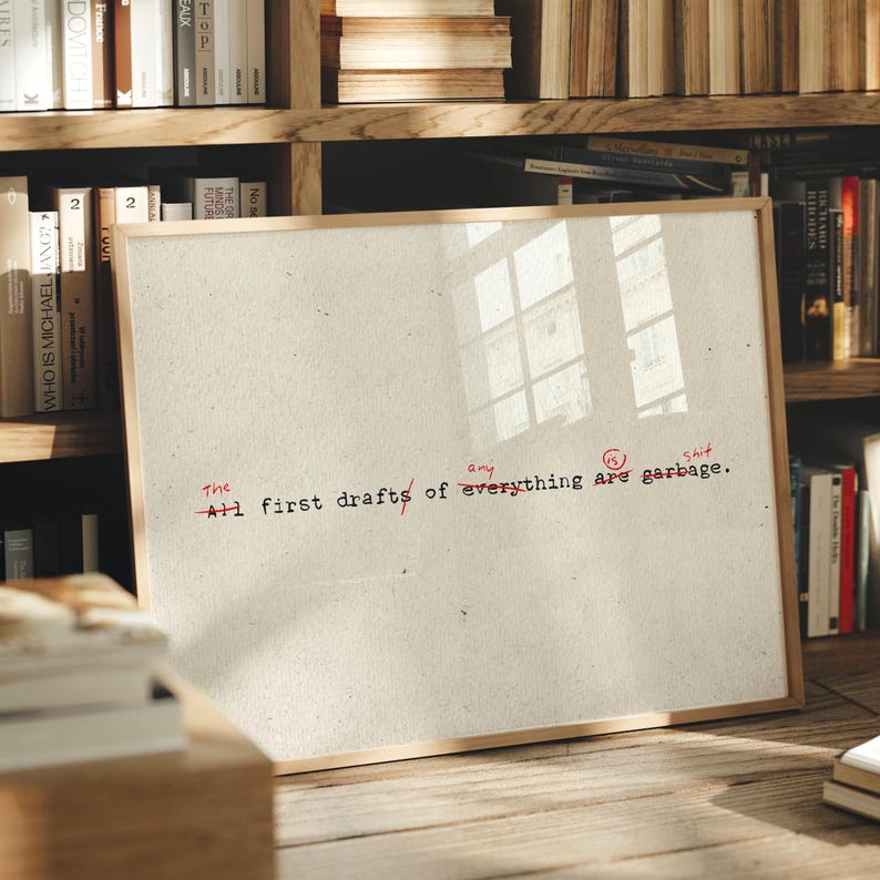 Puede incluir: Una impresi&oacute;n enmarcada con el texto "All first drafts of everything are garbage" en negro y rojo. La impresi&oacute;n est&aacute; en un marco de madera y est&aacute; apoyada contra una estanter&iacute;a llena de libros.