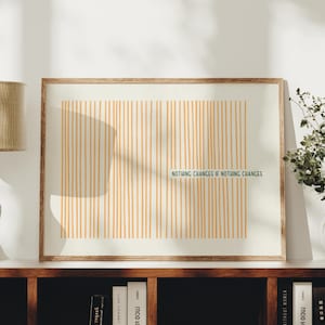 May include: A rectangular framed wall art piece featuring a cream-coloured background with vertical orange lines. The text "NOTHING CHANGES IF NOTHING CHANGES" is printed in dark green letters across the centre of the vertical orange lines.