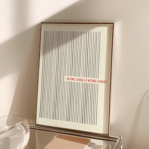 May include: A framed vertical wall art print featuring a series of thin, dark gray vertical lines on a cream background. The text "NOTHING CHANGES IF NOTHING CHANGES" is printed in red, sans-serif capital letters across the center of the lines.