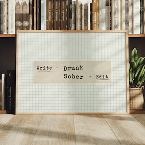 May include: A framed rectangular print featuring a light blue grid pattern on a white background. A central beige rectangular strip displays the black typewriter-style text: Write - Drunk, Sober - Edit, with red underlines.