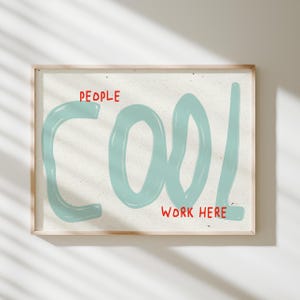 May include: A rectangular framed wall art print featuring a light-colored speckled background. The word COOL is written in large, light blue, hand-drawn style letters. The words PEOPLE and WORK HERE are printed in small, red, sans-serif text.