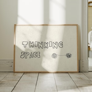 Op de afbeelding: Een ingelijste kunstdruk met de woorden "THINKING SPACE" in zwarte blokletters. Een eenvoudige lijntekening van een spiraal en een wirwar staat rechts van de tekst. De lijst is lichtbruin.