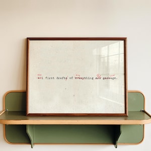 Puede incluir: Una impresi&oacute;n enmarcada con un marco de madera marr&oacute;n. La impresi&oacute;n tiene un fondo blanco con texto rojo que dice "The All first drafts of everything are garbage."