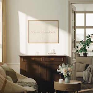 Puede incluir: Un cuadro enmarcado con el texto "Art. First draft of everything are garbage." cuelga sobre un mueble de madera marr&oacute;n oscuro. Una silla de mimbre y una mesa de centro redonda de madera con un jarr&oacute;n de flores est&aacute;n en primer plano.