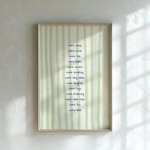 May include: Framed artwork with a light green and white striped background. The artwork features the words "more sleep, more music, more tea, more books, more sunsets, more creating, more long walks, more laughter, more hugs, more dreaming, more road trips, more fun, more love" in blue script.