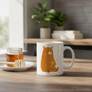 Op de afbeelding: Witte keramische mok met een cartoonbeer die een honingpot vasthoudt. De beer is bruin met een lichtoranje buik en wangen. De mok heeft een gebogen handvat en staat op een houten oppervlak.