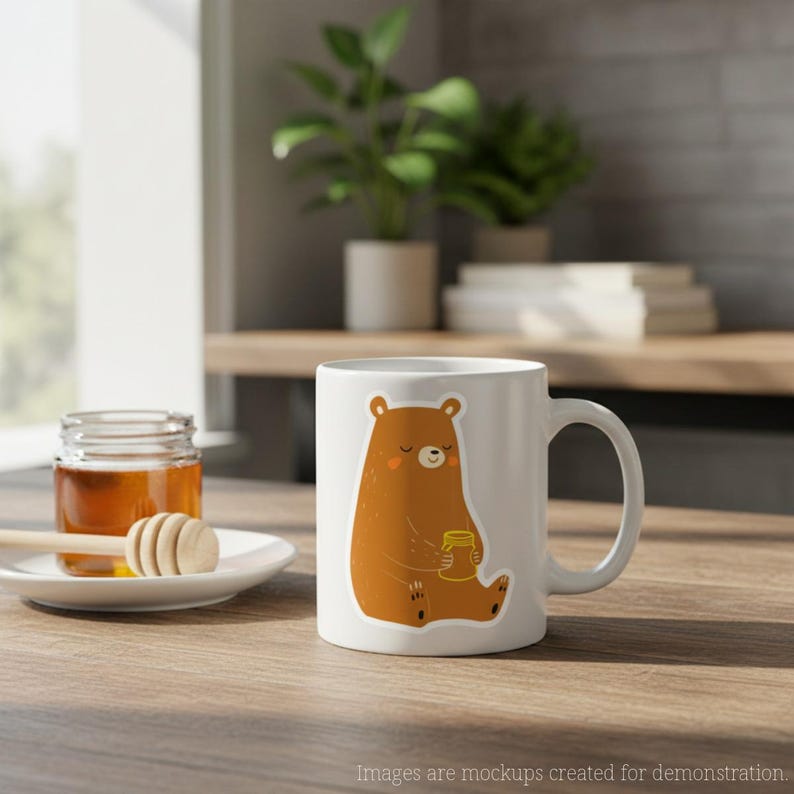 Op de afbeelding: Witte keramische mok met een cartoonbeer die een honingpot vasthoudt. De beer is bruin met een lichtoranje buik en wangen. De mok heeft een gebogen handvat en staat op een houten oppervlak.