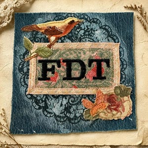 May include: A square denim fabric patch featuring a central rectangular panel with the black embroidered letters FDT. The design includes a yellow and brown bird, a small orange butterfly, green leaves, and a floral pattern over a black lace print.